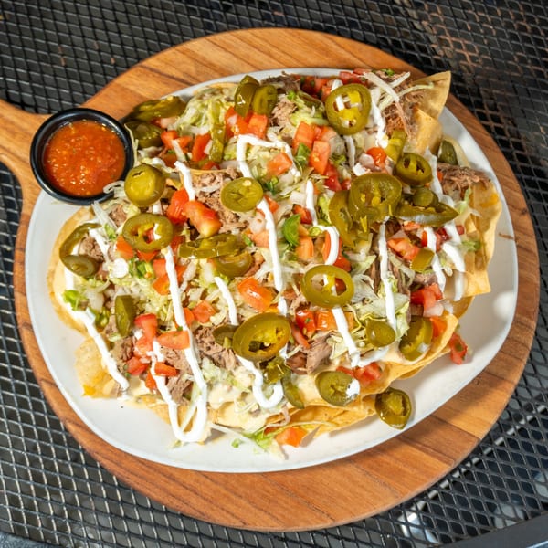 A plate of loaded nachos with shredded meat, cheese, jalapeños, tomatoes, lettuce, and sour cream.