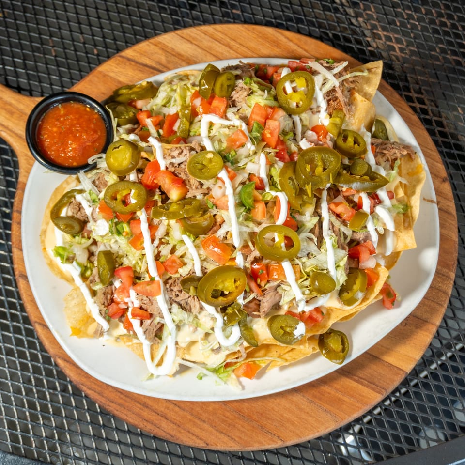 A plate of loaded nachos with shredded meat, cheese, jalapeños, tomatoes, lettuce, and sour cream.