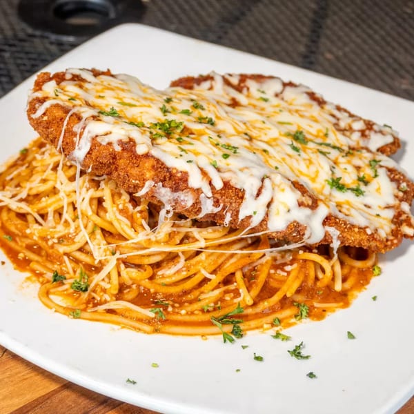 Chicken Parmesan with melted mozzarella cheese and parsley, served over spaghetti with red sauce.