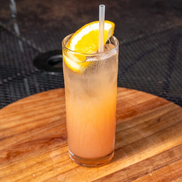 A refreshing orange cocktail with ice and an orange slice, served on a wooden board.