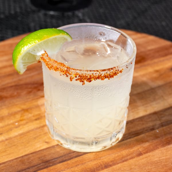 A refreshing cocktail with a chili-lime rim and a lime wedge, on a wooden surface.