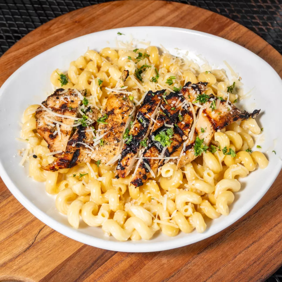 Grilled chicken slices over macaroni and cheese, garnished with parsley and grated cheese.