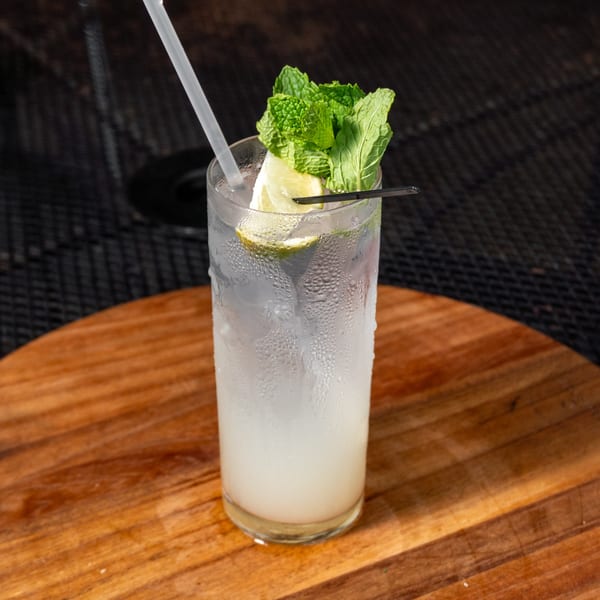A tall, frosted glass of mojito with lime, mint, and a straw on a wooden table.