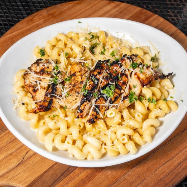Grilled chicken and cavatappi pasta with parmesan cheese and parsley on a white plate.