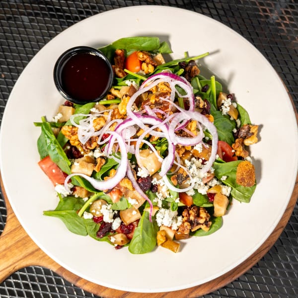 Spinach salad with walnuts, cranberries, feta, red onion, and pear, with a side of dressing.