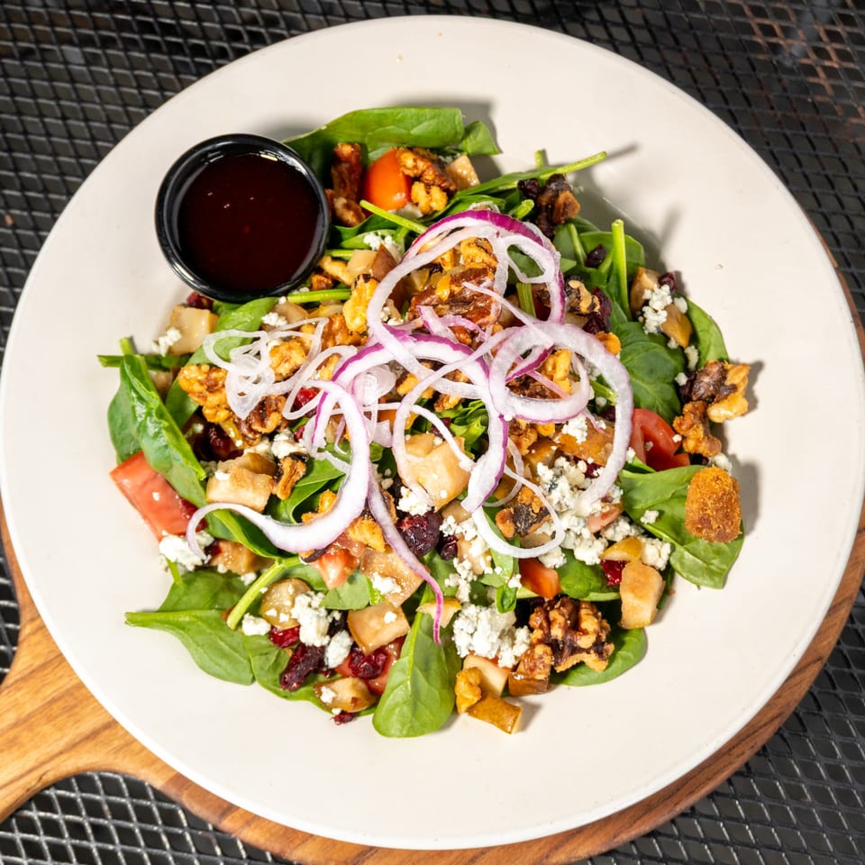 Spinach salad with walnuts, cranberries, feta, red onion, and pear, with a side of dressing.